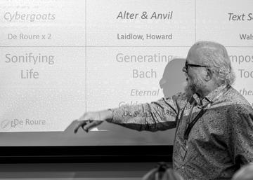Dave De Roure stands in front of a projector screen, pointing at a square with the text 'Sonifying Life'